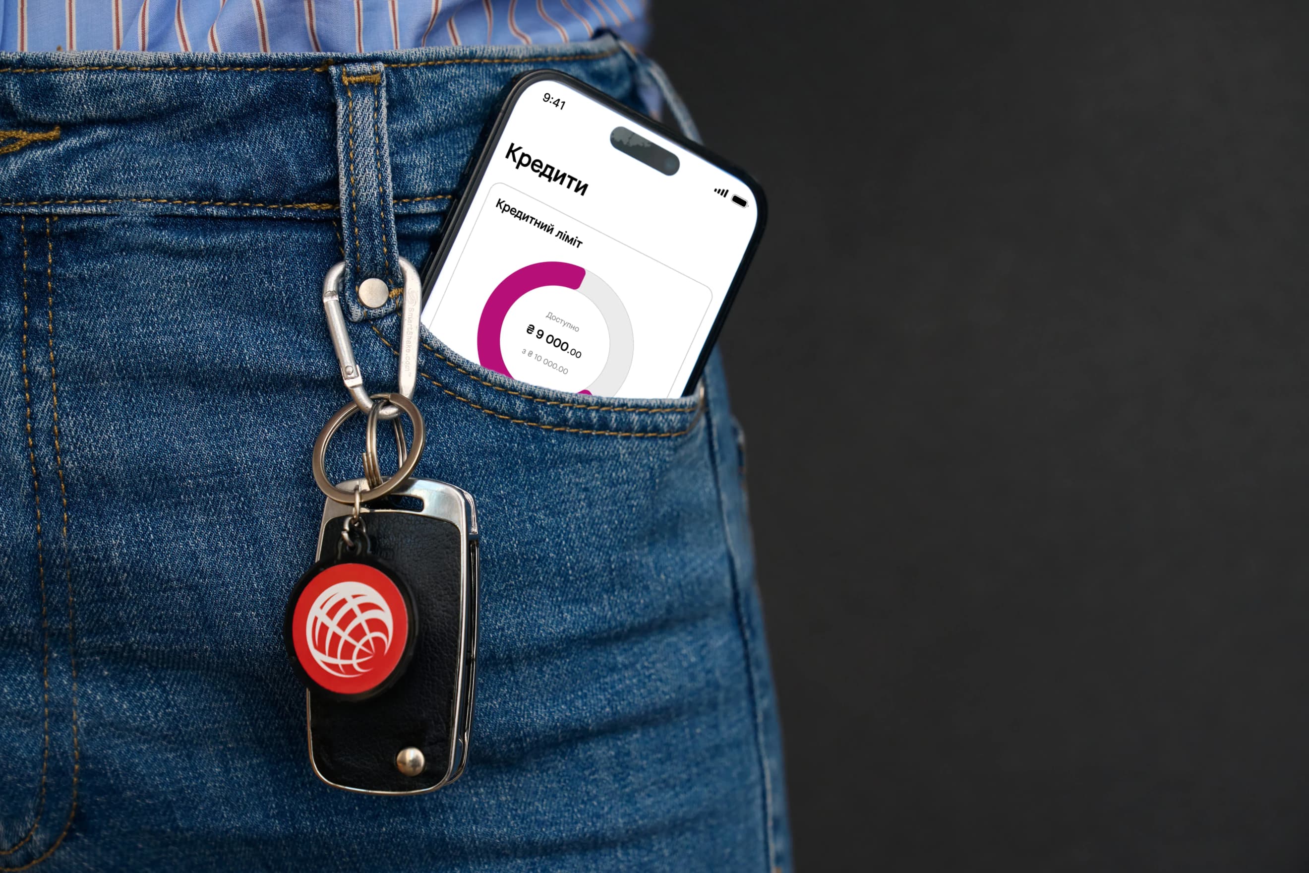 Смартфон із розділом «Кредити» застосунку ProCredit Bank стирчить із джинсової кишені поруч із брелоком для ключів Смартфон із розділом «Кредити» застосунку ProCredit Bank стирчить із джинсової кишені поруч із брелоком для ключів